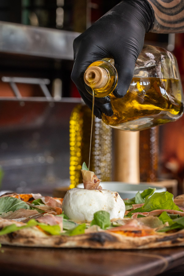 Toque final de aceite de oliva extra virgen sobre pizza burrata con prosciutto y arúgula